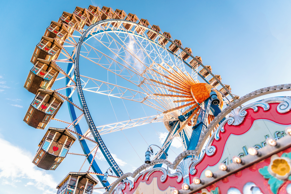 Ferris wheel at an outdoor fair, representing location-based entertainment with its vibrant, traditional gondolas against a clear blue sky.